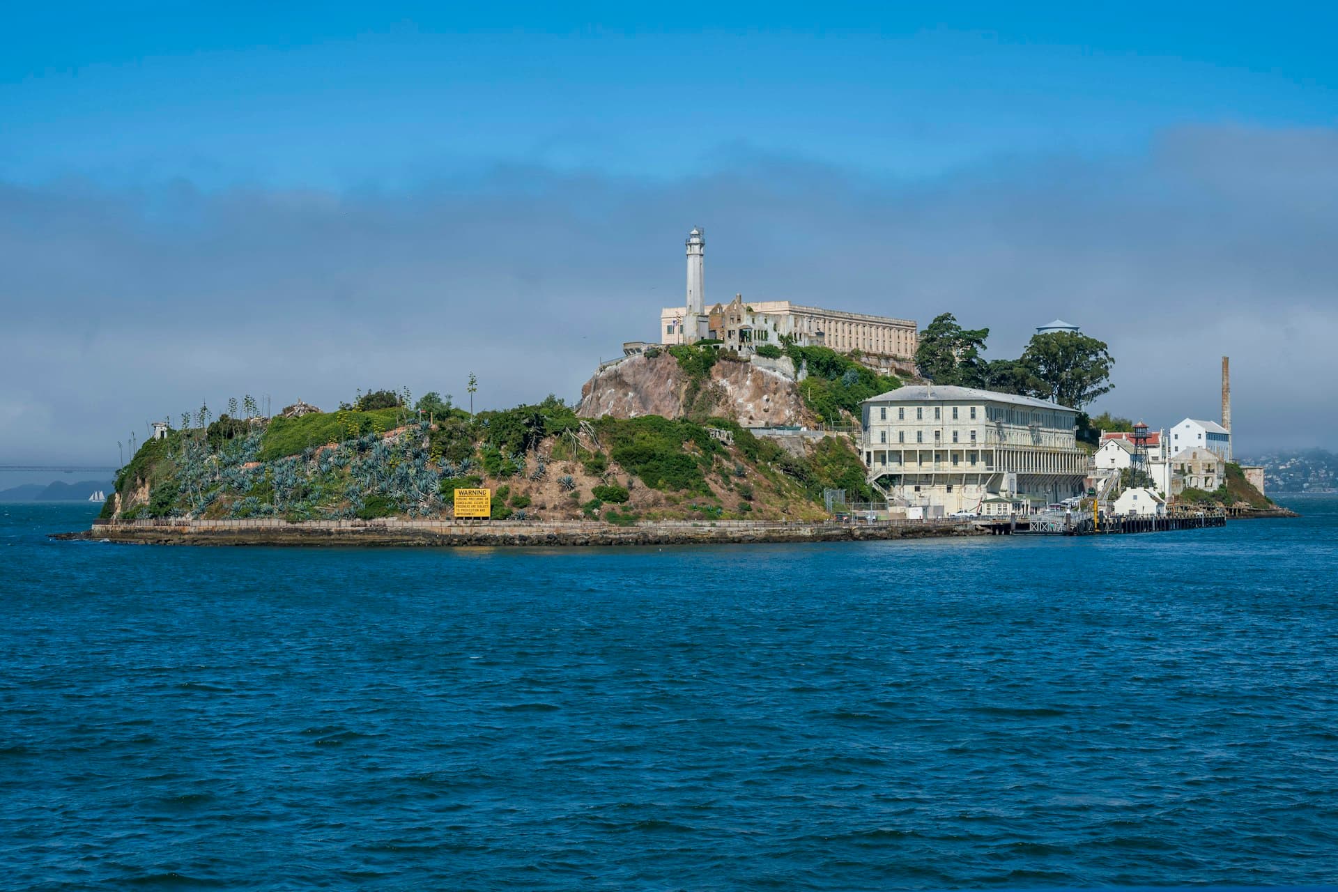 Alcatraz Island with lighthouse and historic prison buildings viewed from San Francisco Bay under sunny skies