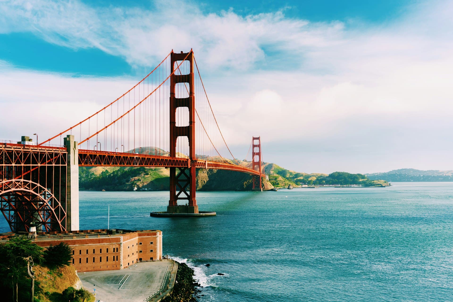 Golden Gate Bridge spanning San Francisco Bay with blue water and clear sky, historic brick fort visible in foreground.