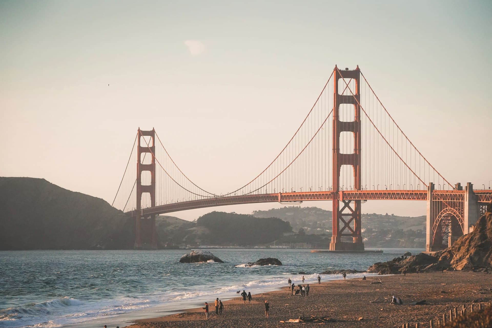 Visitors enjoying a beach with the Golden Gate Bridge spanning across the bay at golden hour