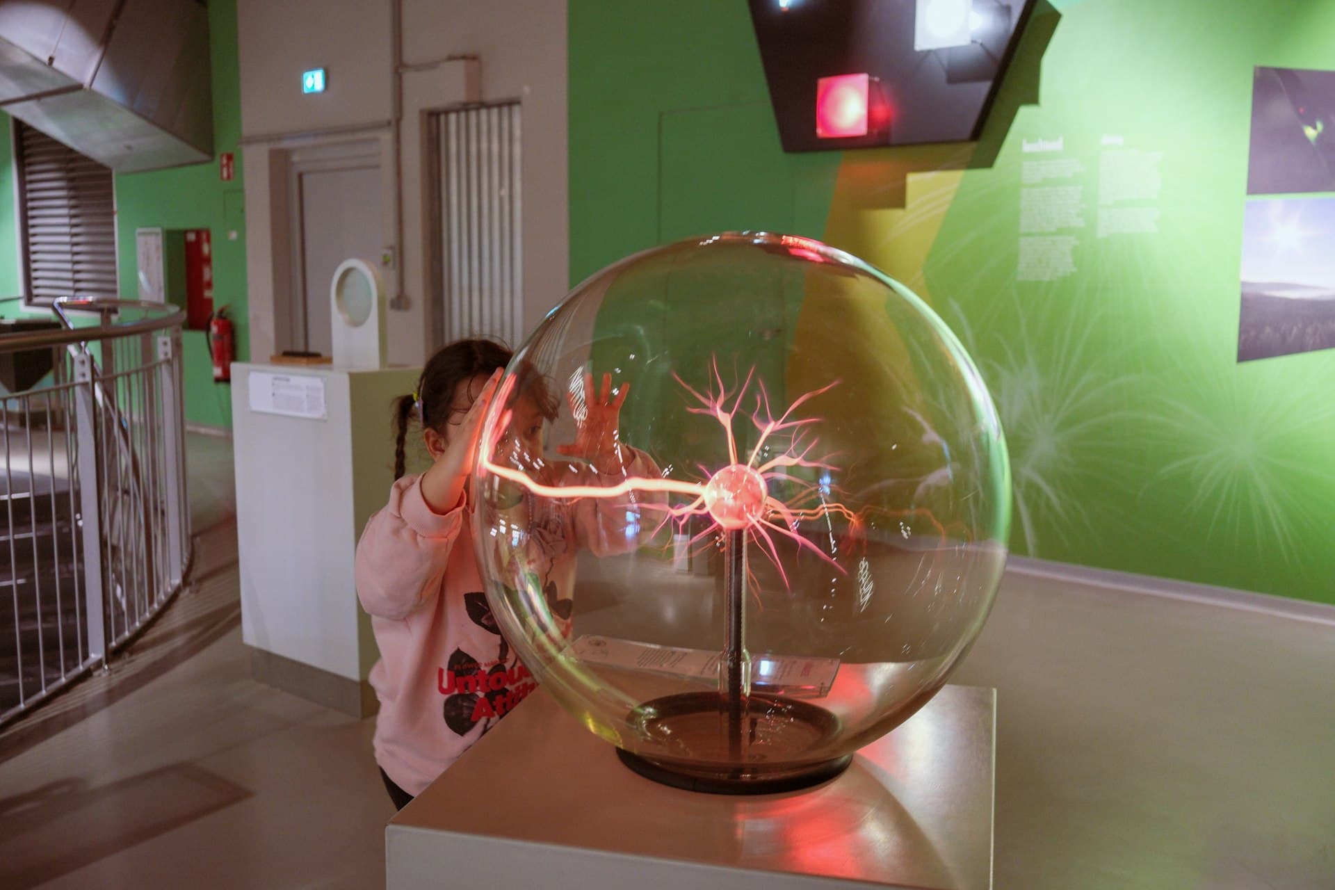 Child in pink hoodie touching an illuminated plasma ball display in a science museum
