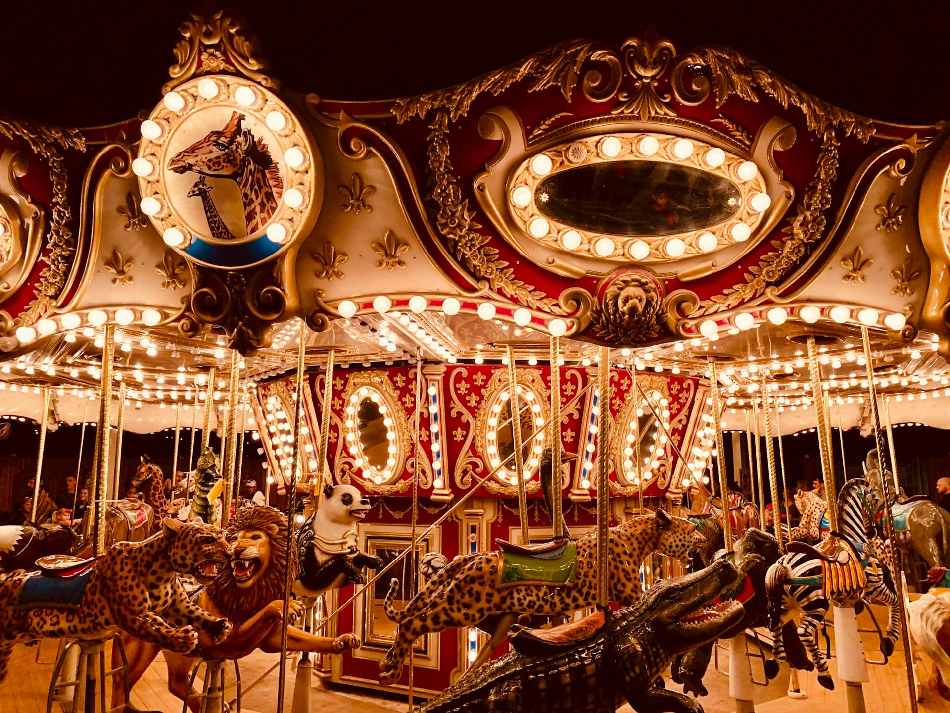 Vintage illuminated carousel at night with ornate gold and red details, decorated carousel animals, and glowing lights creating a magical carnival atmosphere.