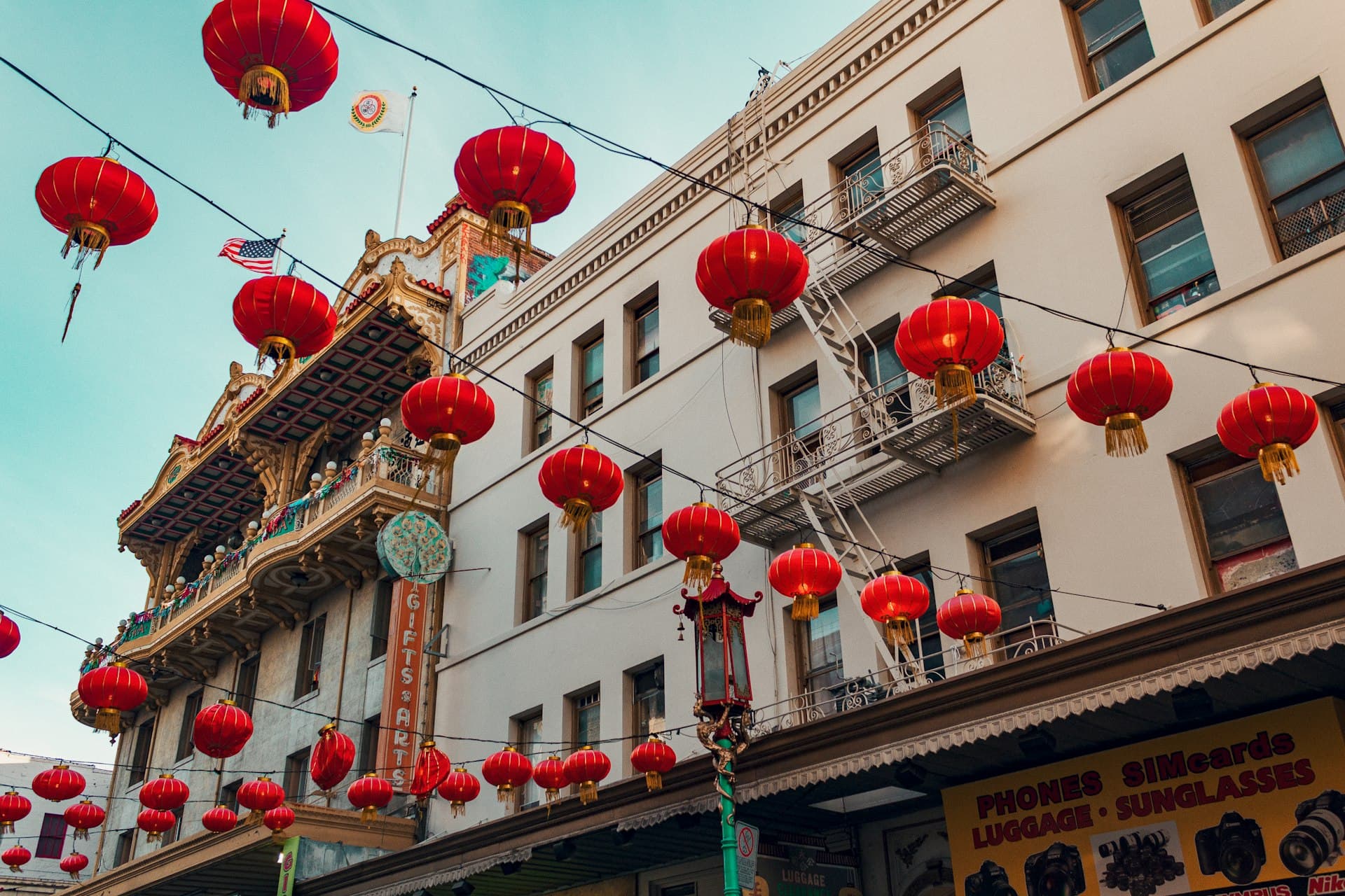 Red paper lanterns strung across historic Chinatown buildings under a clear blue sky