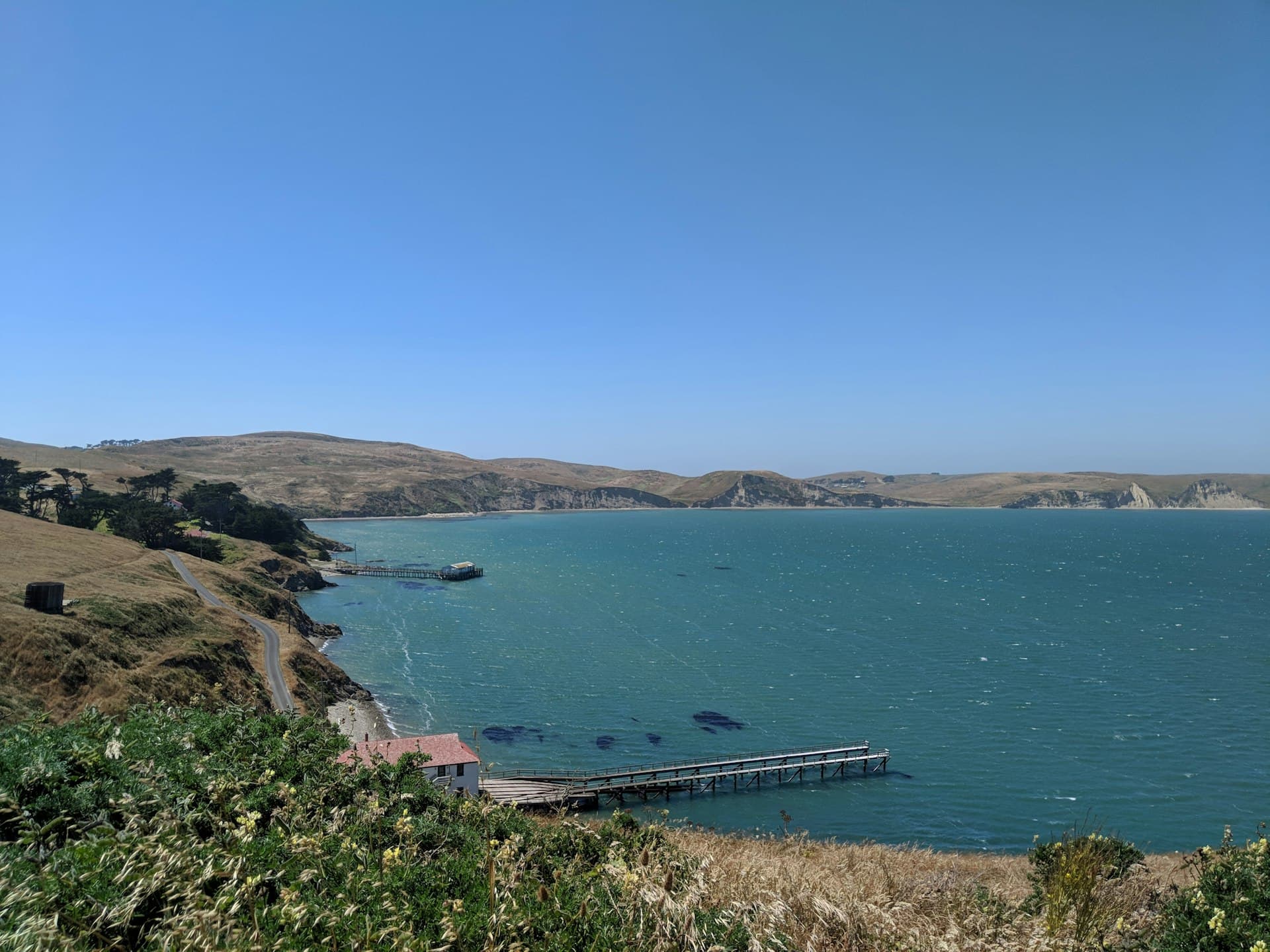 Panoramic view of a turquoise coastal bay with golden hillsides, wooden piers, and clear blue skies