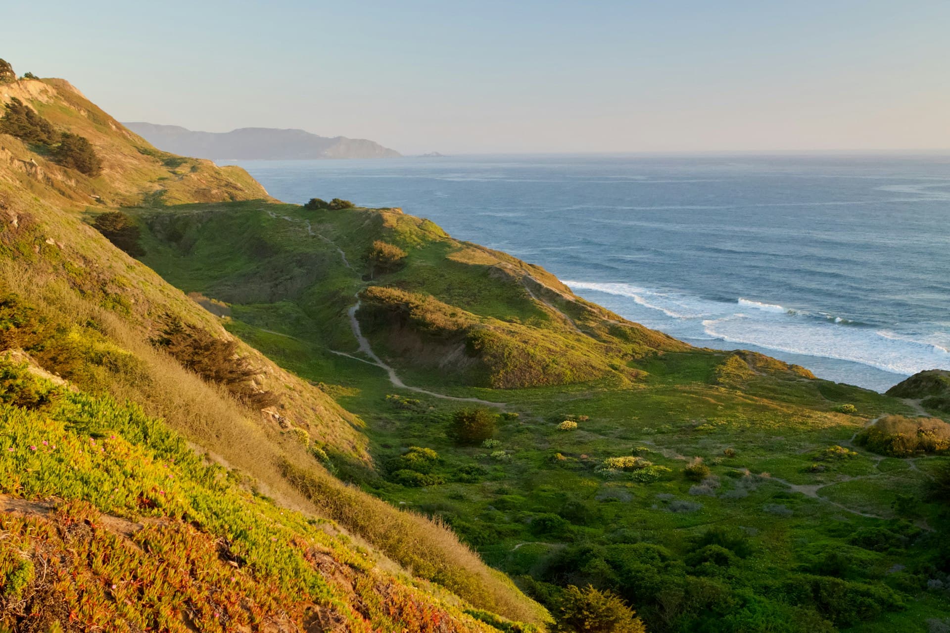Scenic coastal hiking trail with green rolling hills overlooking the ocean at golden hour