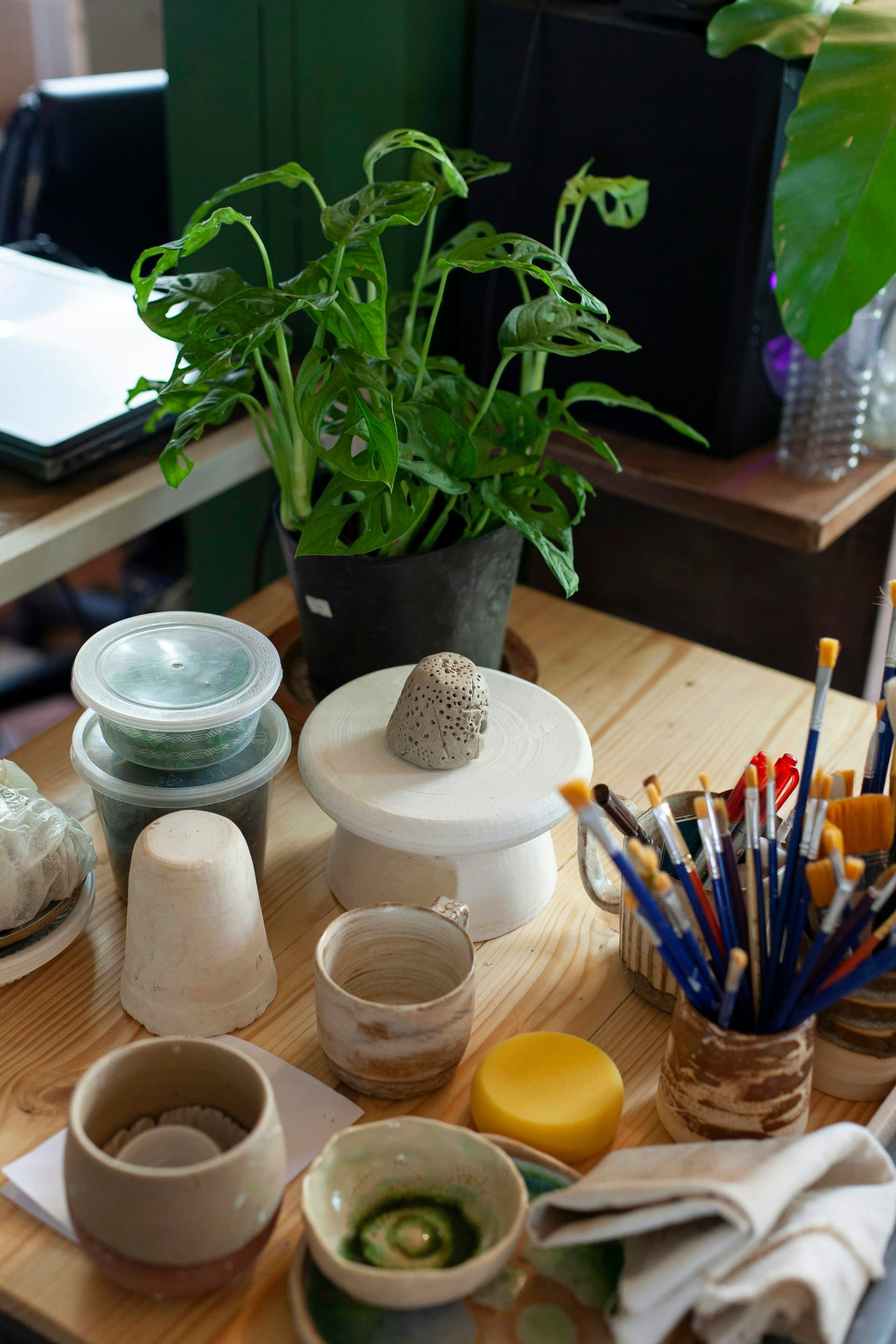 Overhead view of a craft workspace with art supplies, potted plant, and ceramics on a wooden table during an indoor creative activity.