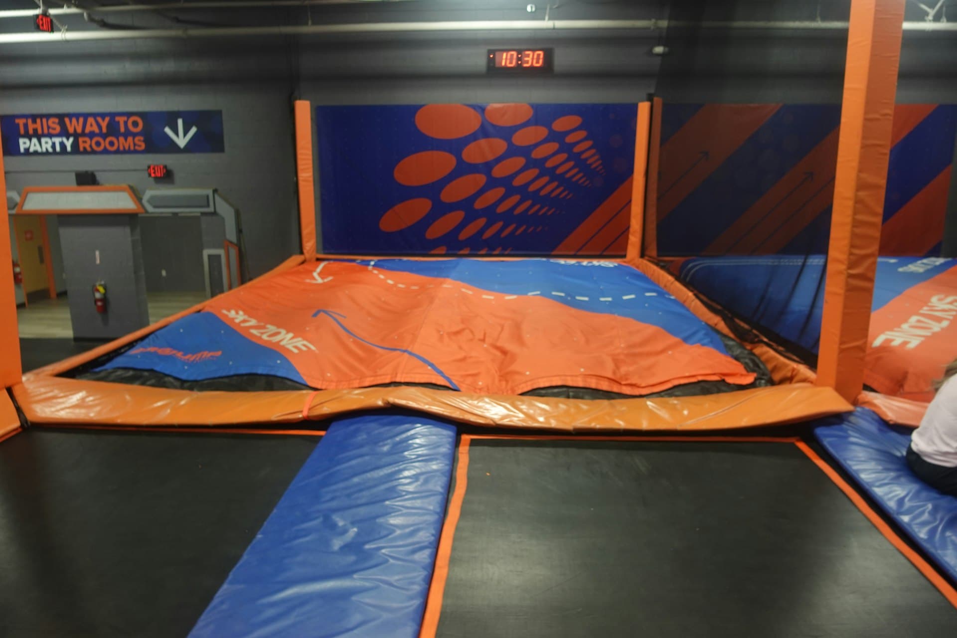 Empty trampoline park with orange and blue padded jumping surfaces and climbing equipment ready for active play.