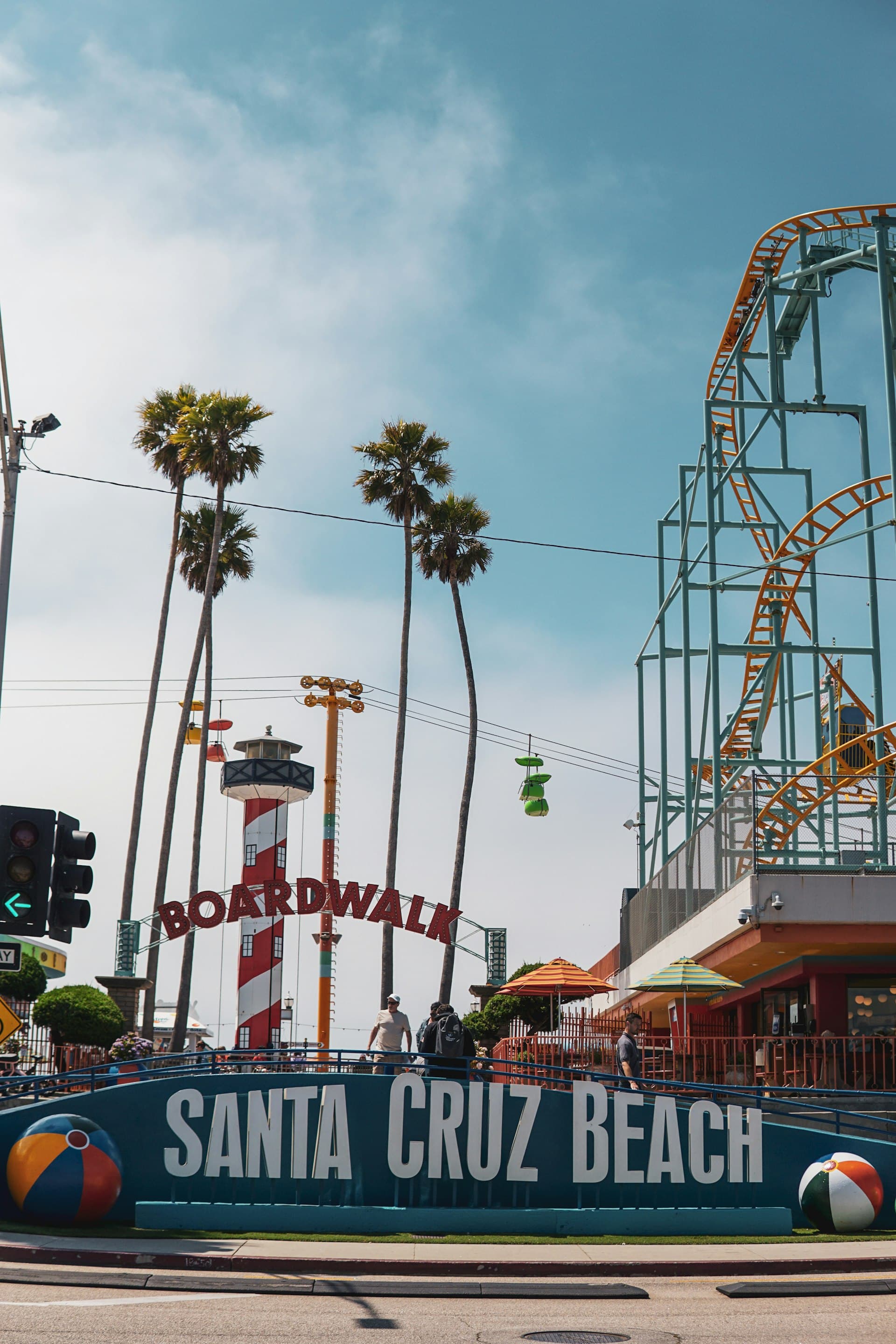 Santa Cruz Beach Boardwalk entrance with red lighthouse, roller coaster, and palm trees on a sunny day.