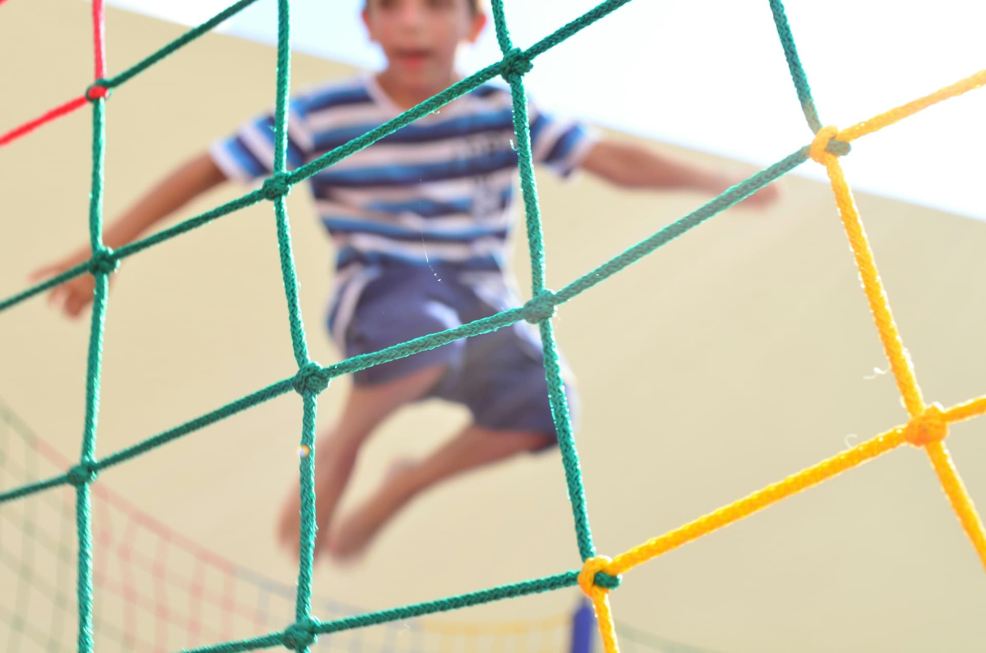 Child climbing on a colorful rope net structure at an outdoor playground on a sunny day